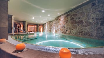Una piscina interior con paredes de piedra, suelo de baldosas e iluminación empotrada en el techo.