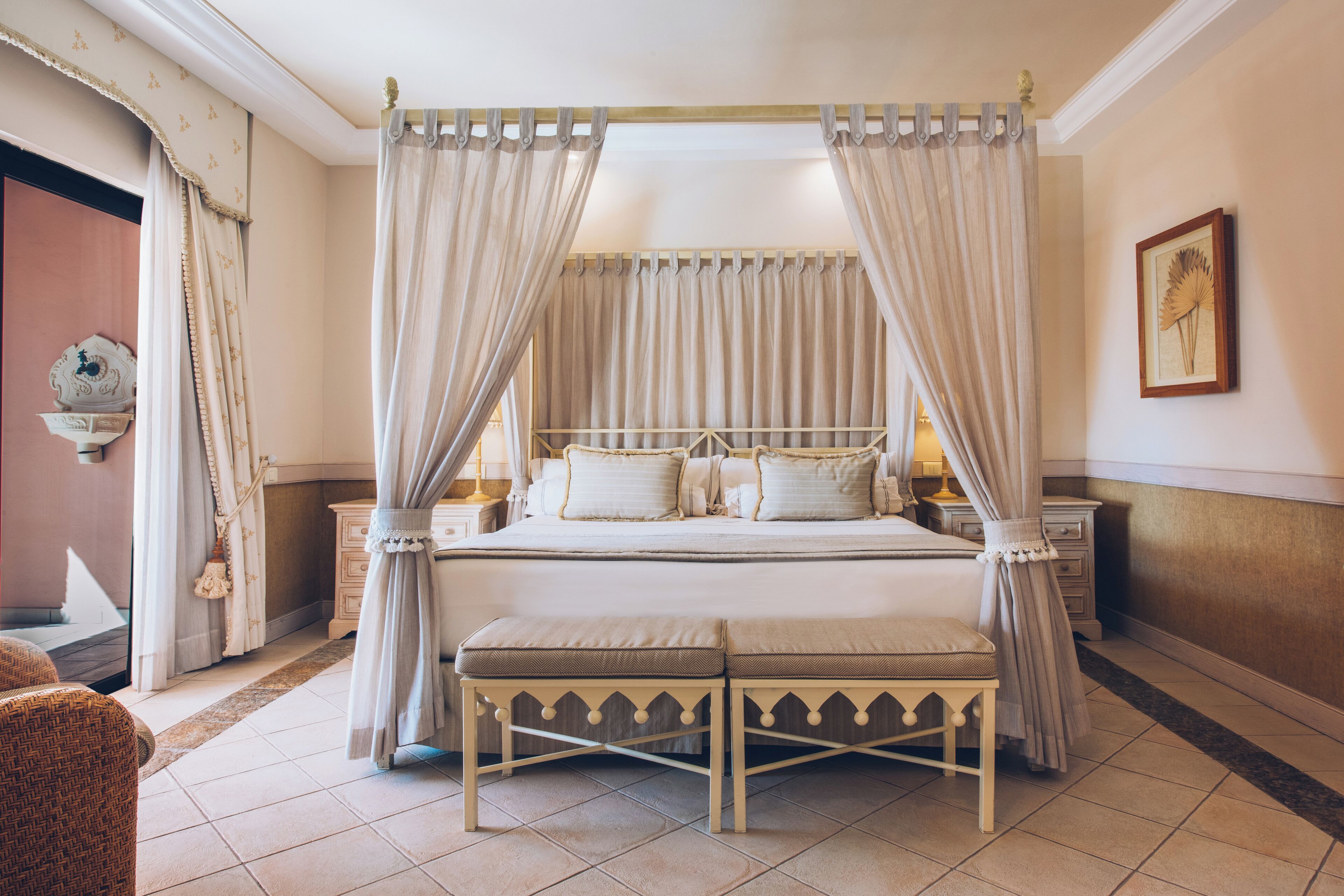 A four-poster canopy bed with a matching bench, a bedside table, and a wall-mounted lamp.