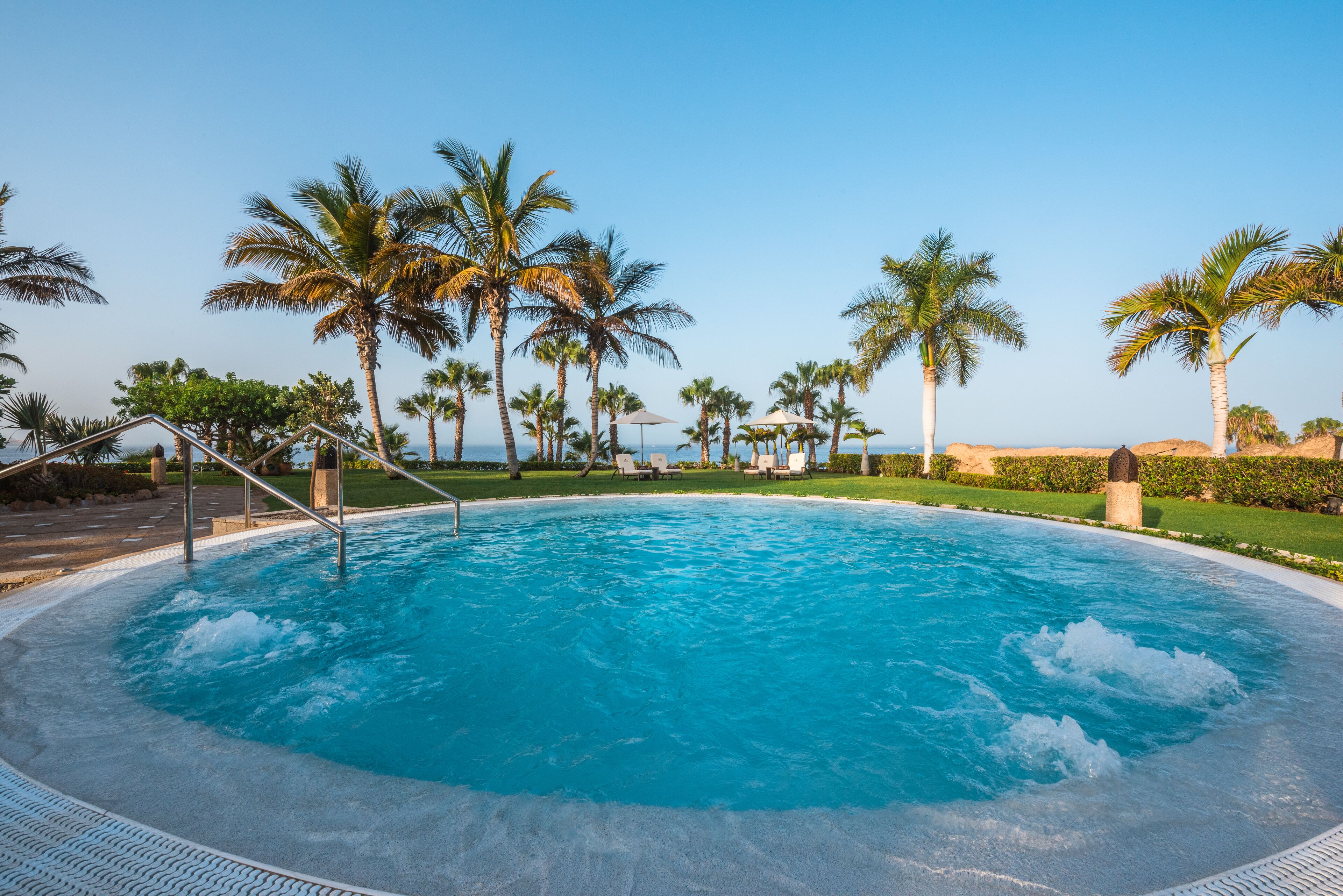 A swimming pool surrounded by palm trees and lounge chairs.