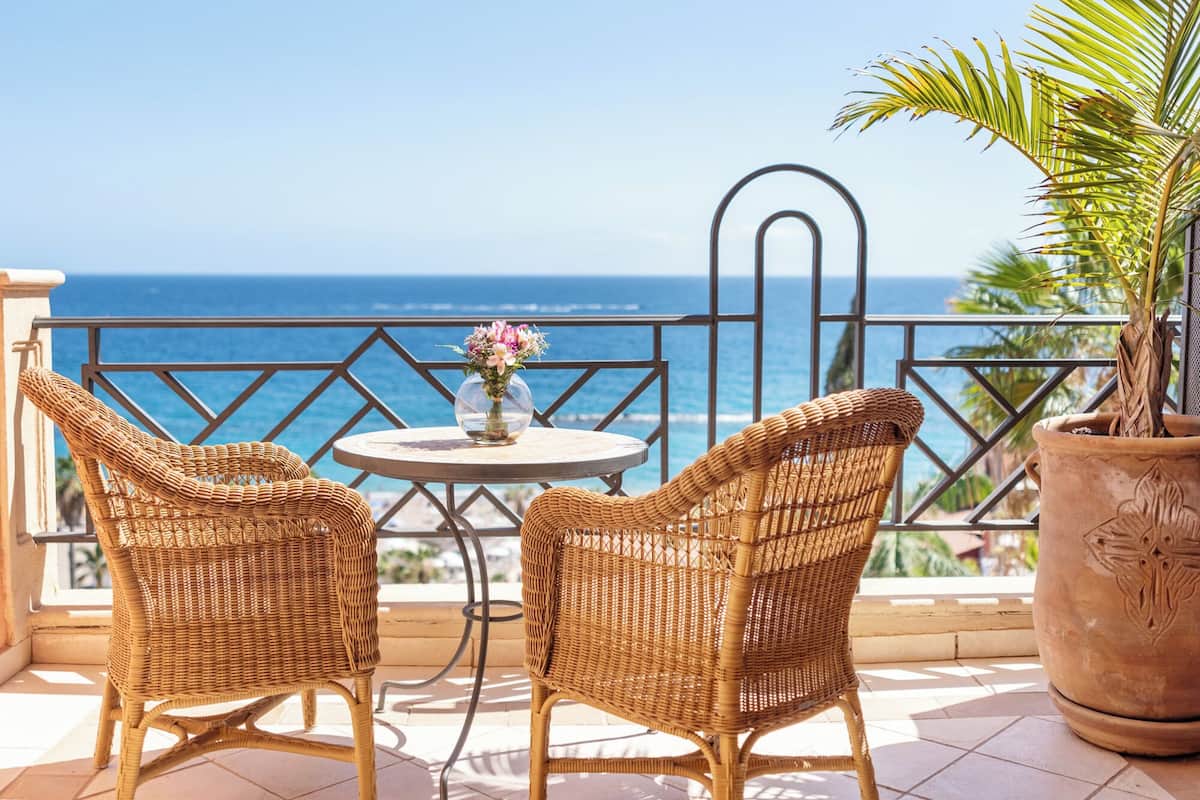 Un balcon avec des fauteuils en osier, une petite table ronde et une plante en pot.