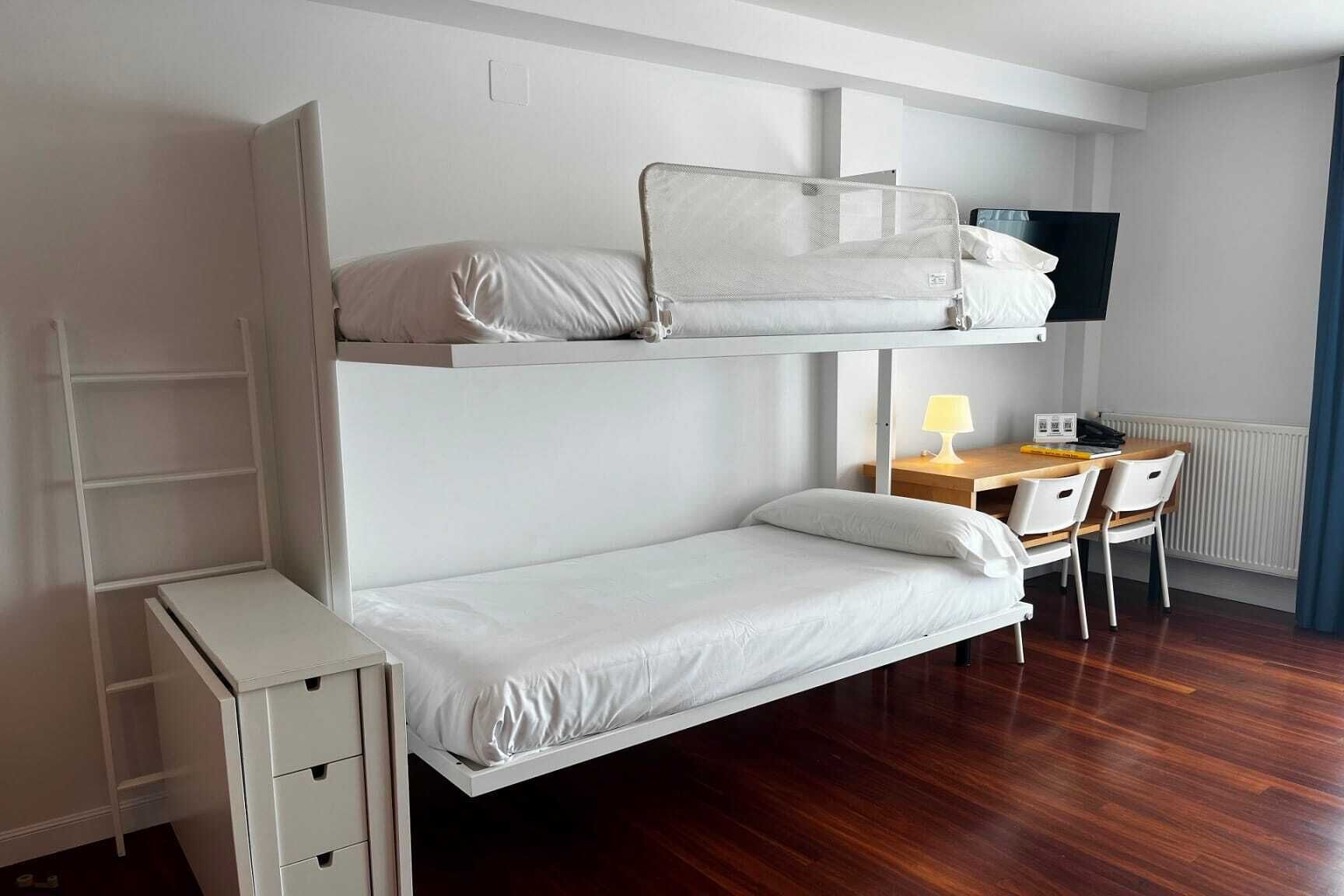 Una cama litera con escritorio y silla, un mueble pequeño y un televisor.