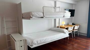 Una cama litera con escritorio y silla, un mueble pequeño y un televisor.