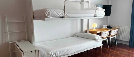 Una cama litera con escritorio y silla, un mueble pequeño y un televisor.
