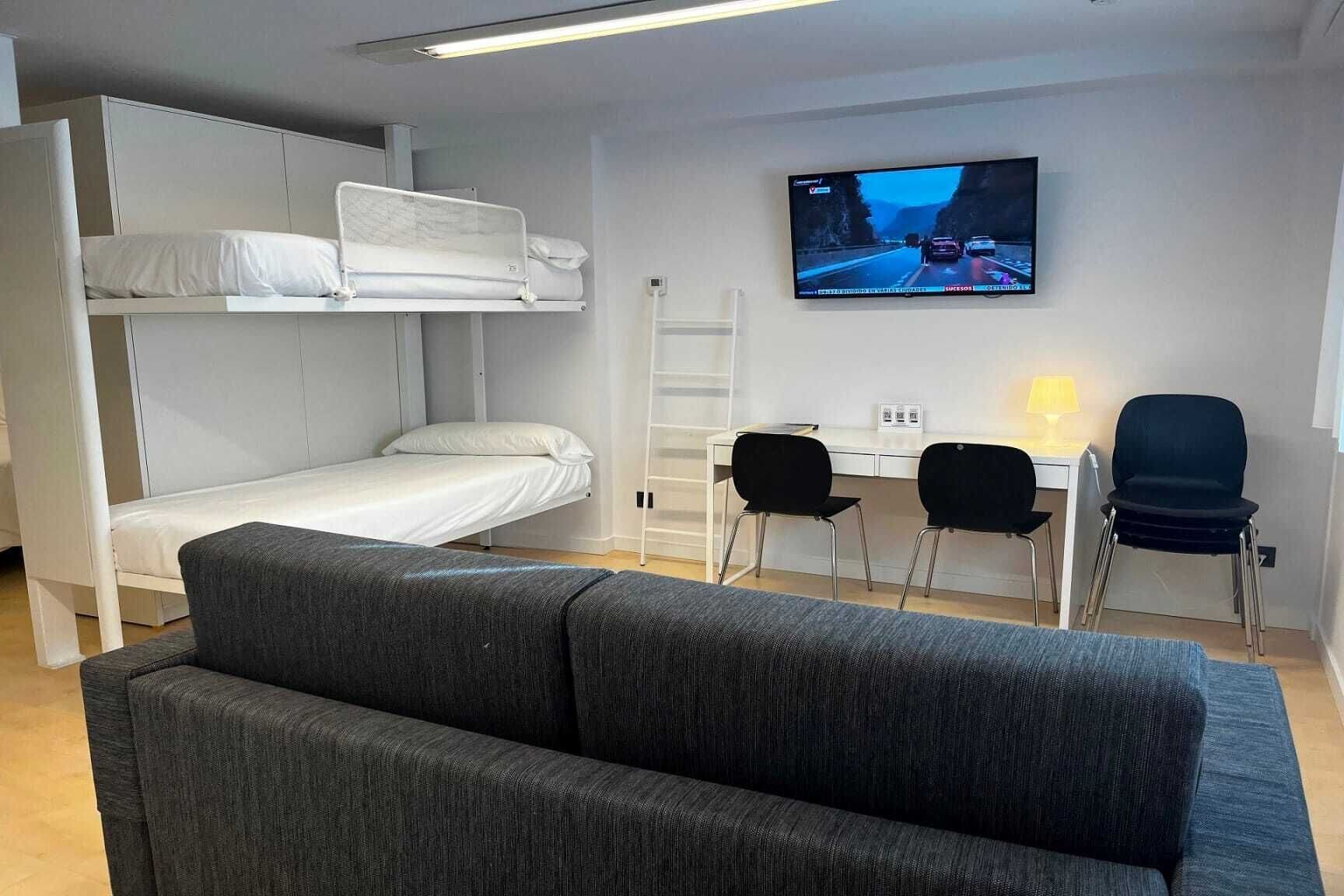 A compact room with bunk beds, a desk, two chairs, a television, and a sofa.