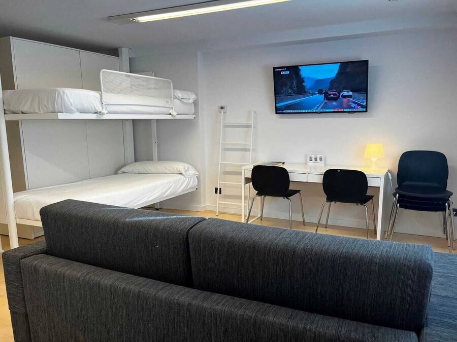 Une pièce de taille modeste, équipée de lits superposés, d’un bureau, de deux chaises, d’une télévision et d’un canapé.