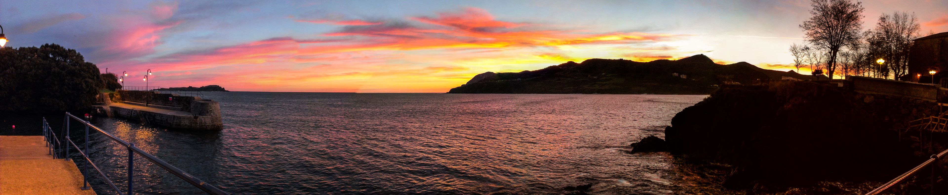 A coastal sunset with a pier and rocky shoreline.