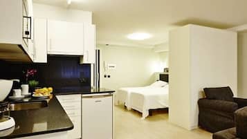 Ein kompaktes Hotelzimmer mit Küchenzeile, einem Einzelbett, einer kleinen Sitzecke und einem separaten Schlafbereich.