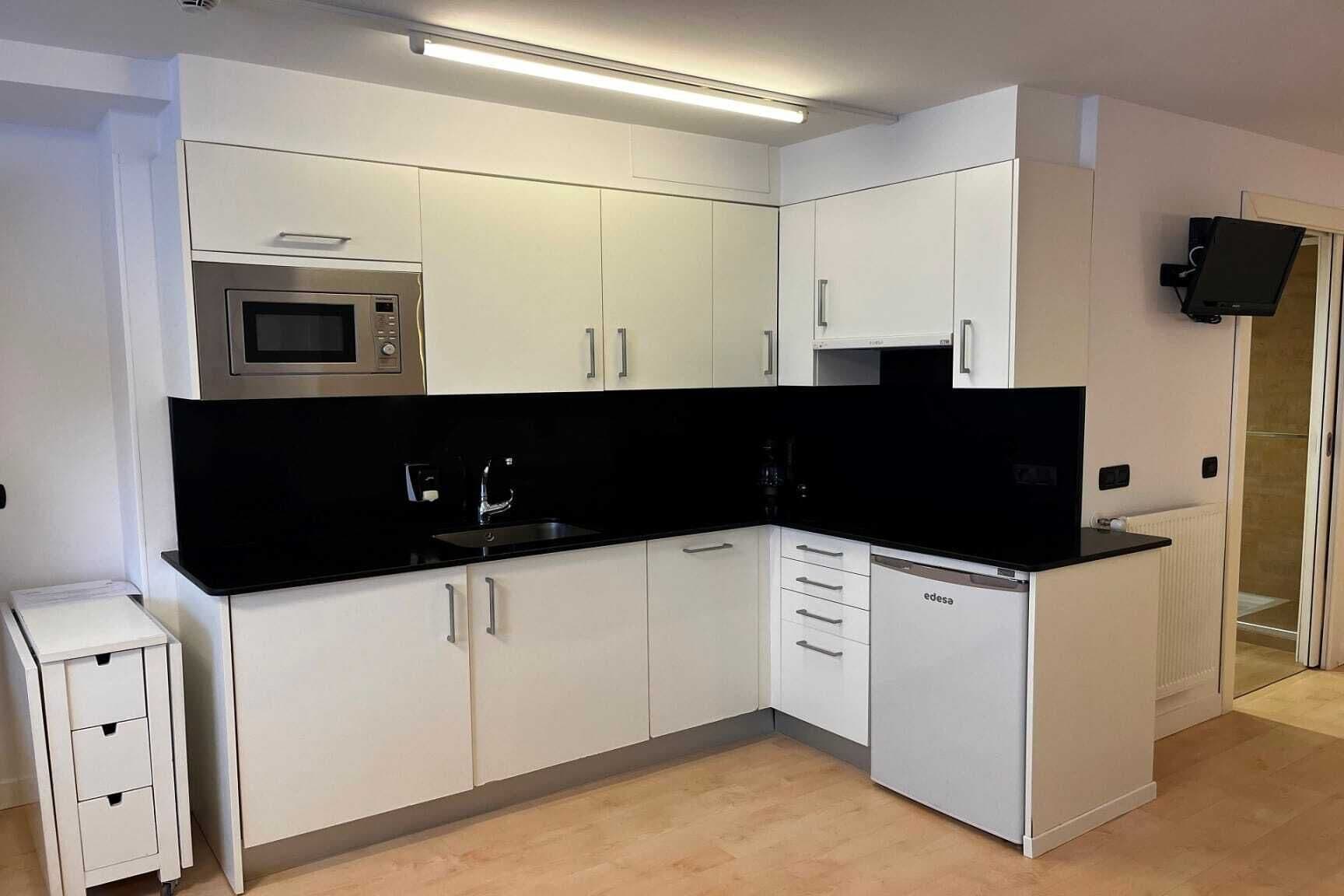 A compact kitchen with white cabinets, a black countertop, a microwave, and a dishwasher.