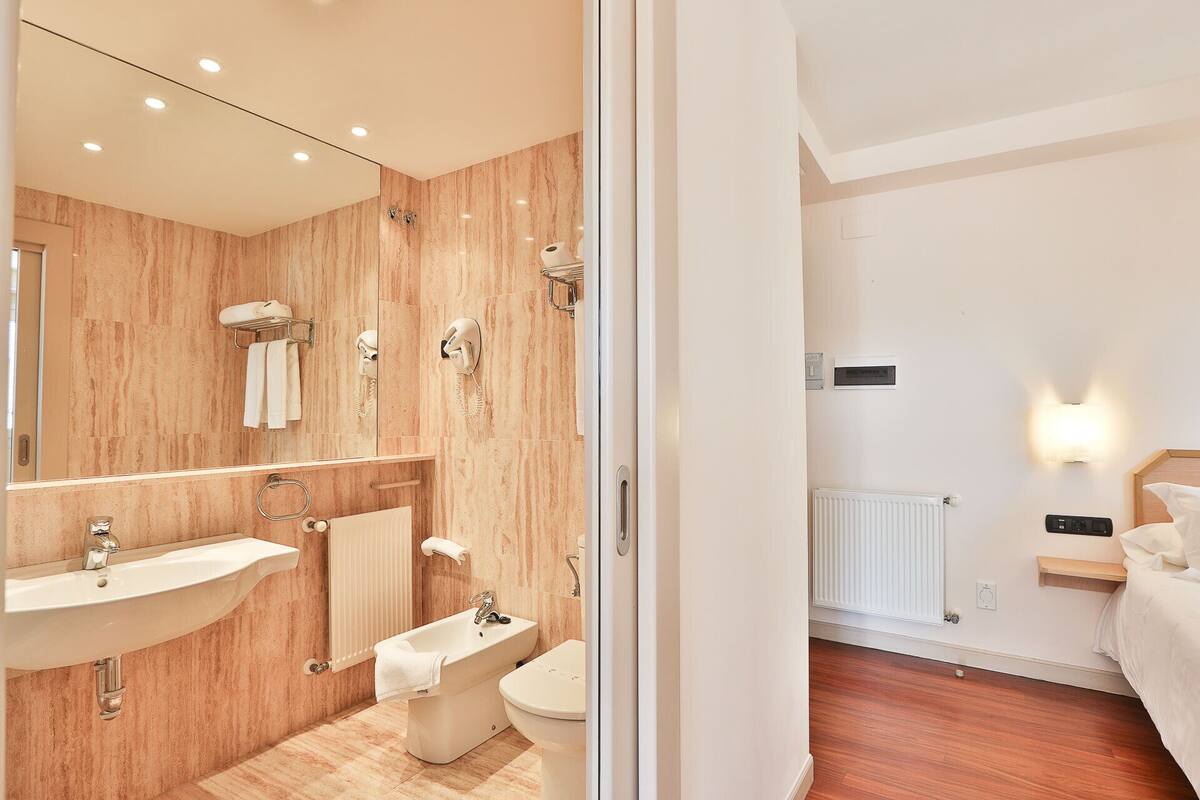 A modern bathroom with a sink, bidet, and toilet, wooden walls, and a mirror.