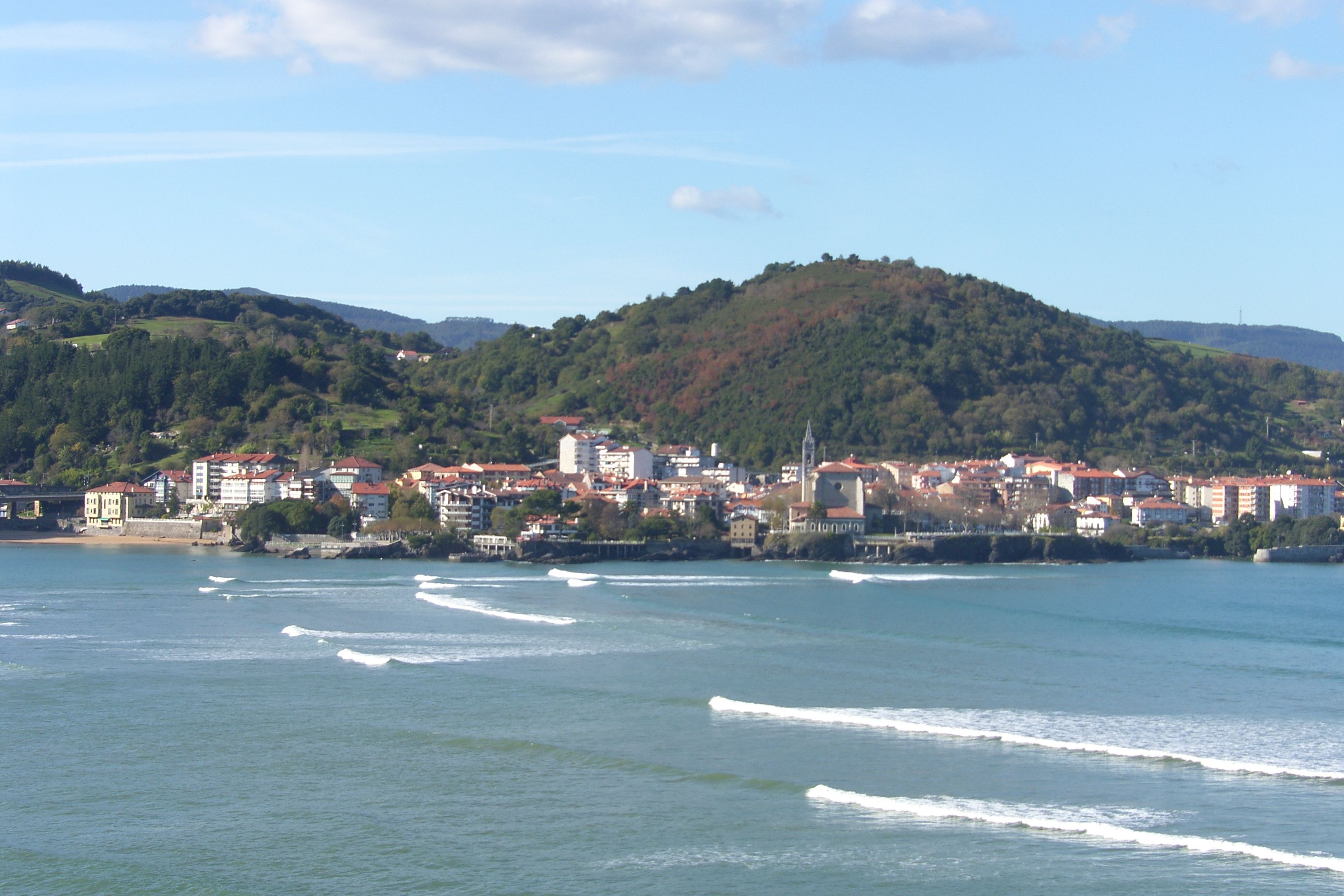 A coastal town with buildings along the shoreline and a hill in the background.