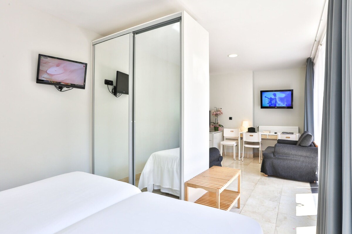 A modern hotel room with a bed, a desk, a chair, and a TV.