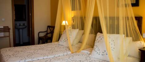 A double bed with a canopy, a bedside table, a chair, and a mirror.