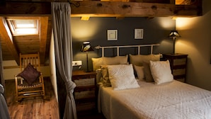 Un dormitorio acogedor con techo de madera, una cama con ropa de cama blanca, una mesita de noche con una lámpara y un sillón con cojín.