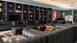 Een moderne woonkamer met zwarte leren banken, een grote flatscreen televisie en diverse decoratieve items op planken.