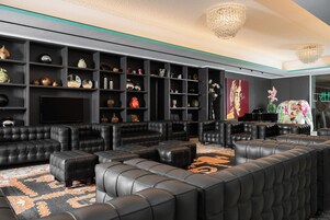 A modern living room with black leather sofas, a large flat-screen TV, and a variety of decorative items on shelves.