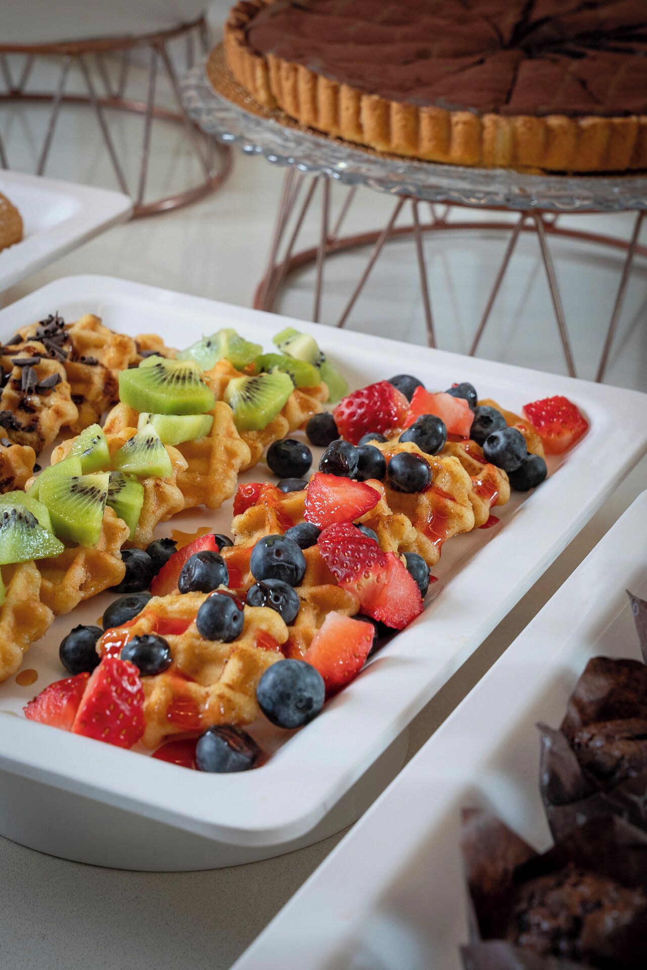Een plateau met desserts, met wafels belegd met aardbeien, blauwe bessen en kiwischijfjes.