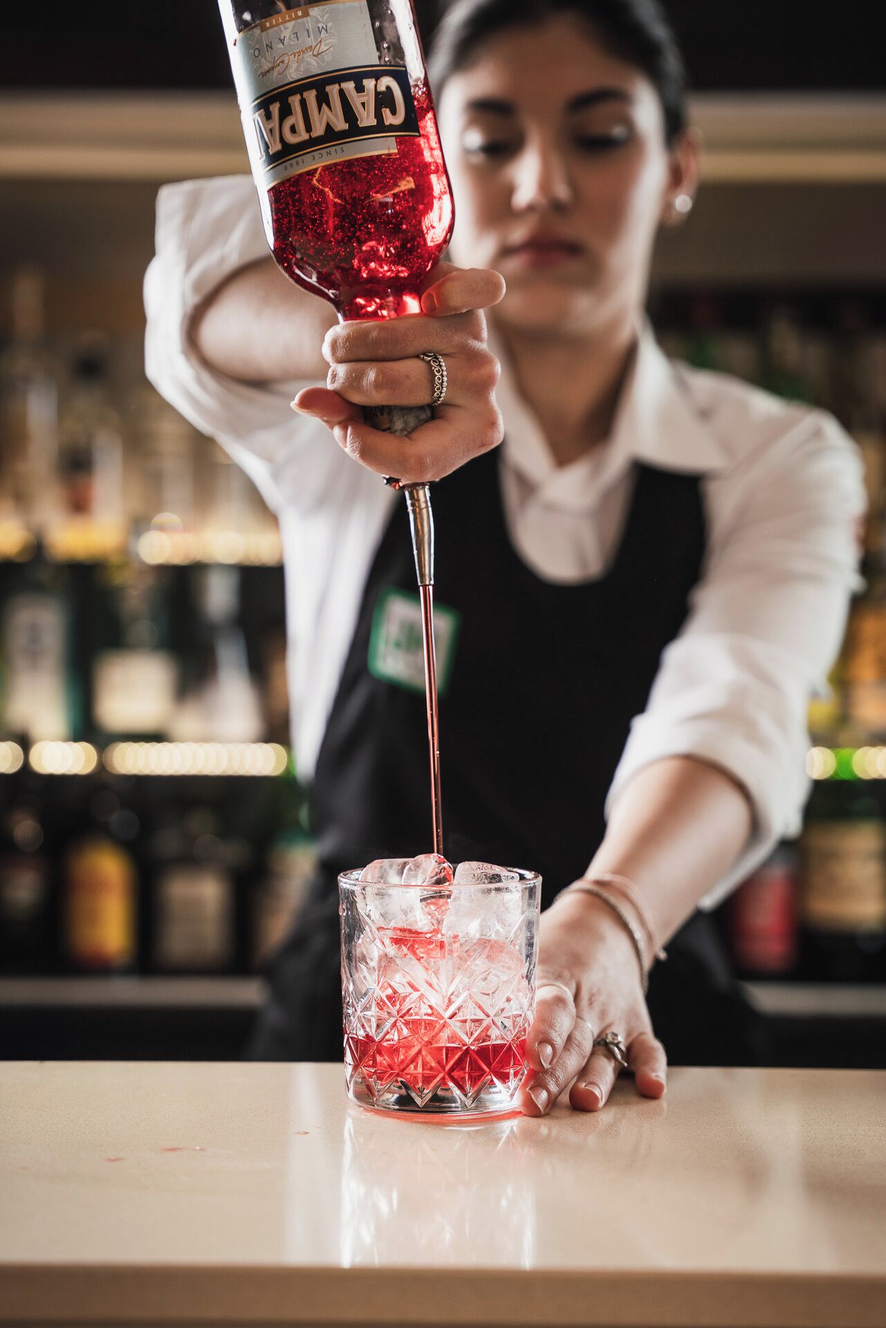 Un barman verse une boisson rouge dans un verre transparent orné d’un motif en losanges.