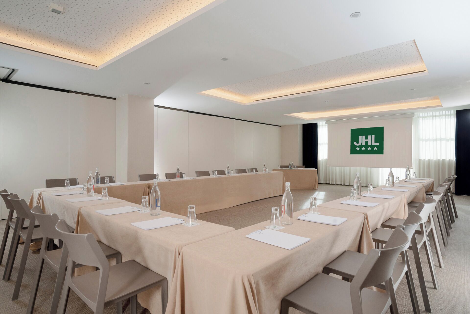 A conference room with a long table, chairs, and a JHL logo on the wall.