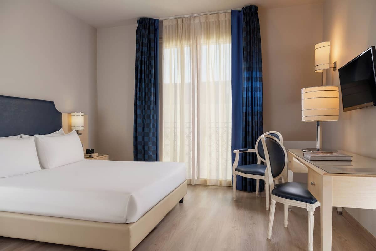 A hotel room with a bed, a desk, a chair, a TV, and curtains.