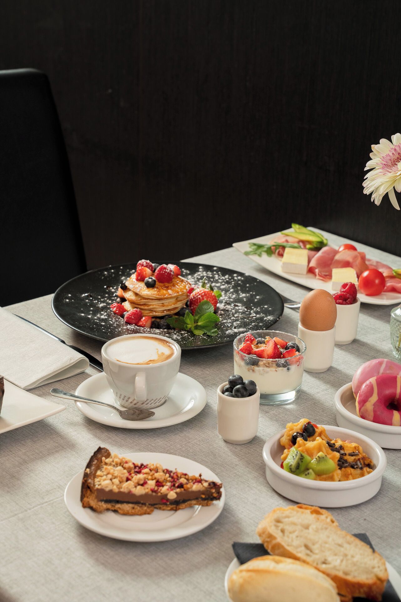 Un desayuno con tortitas, café, yogur y diversas pastas sobre una mesa.