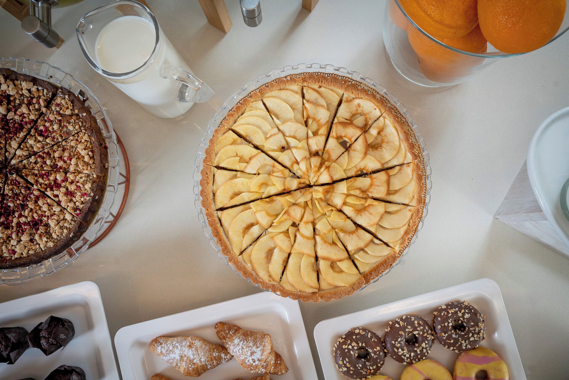 A table with a variety of desserts including a pie with apple slices, a chocolate-covered pastry, and a plate of chocolate donuts.