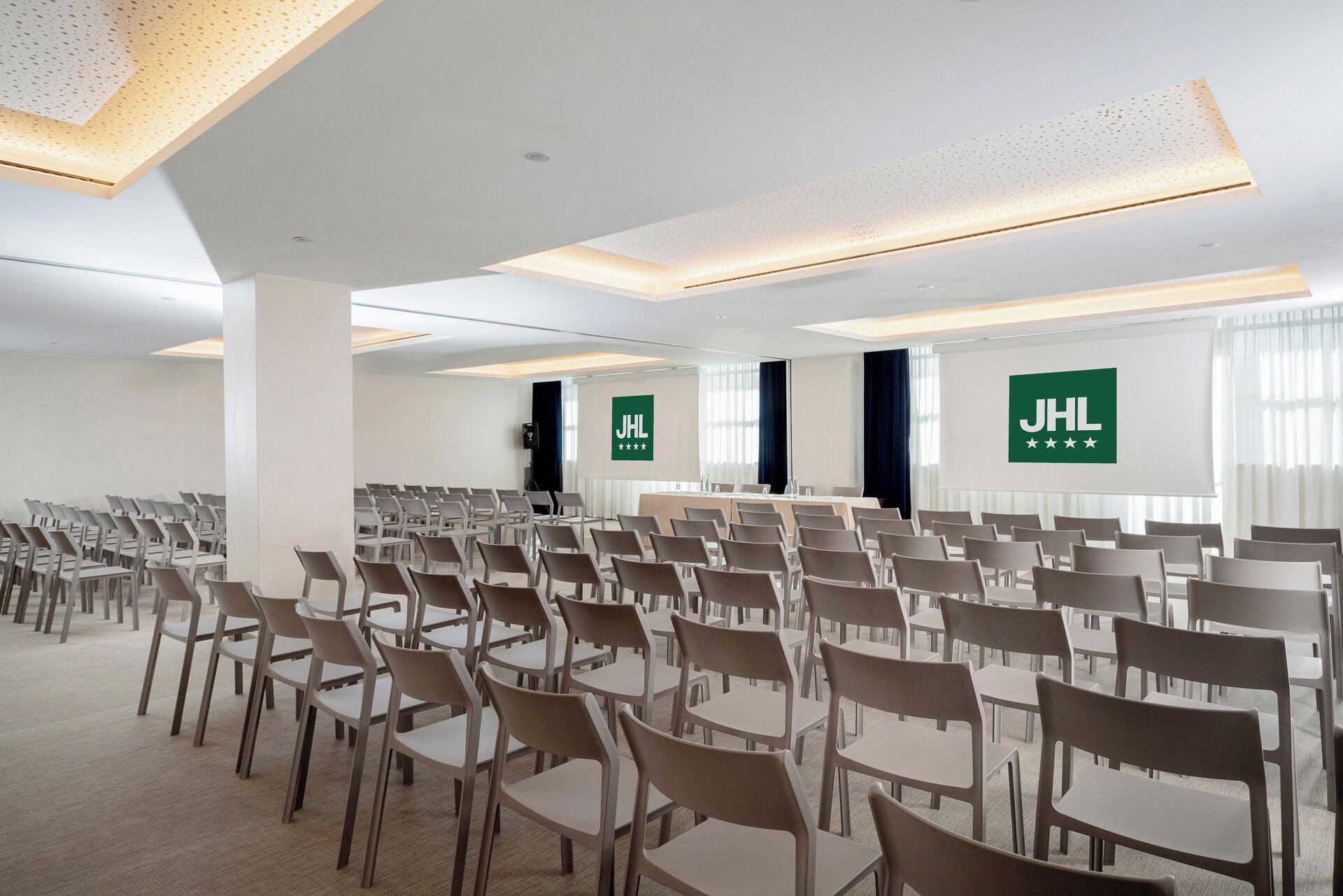 Una sala conferenze con file di sedie e tavoli, pareti bianche e luci a soffitto.