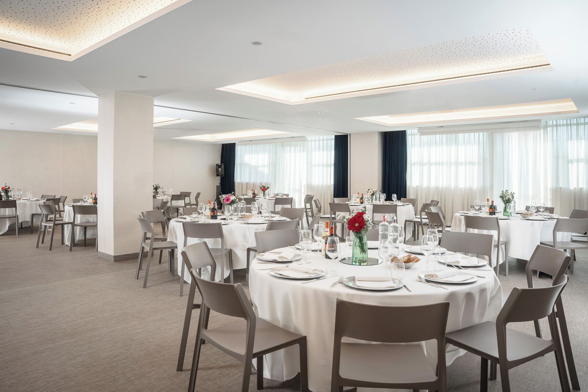 A spacious conference room with round tables, white tablecloths, and grey chairs.