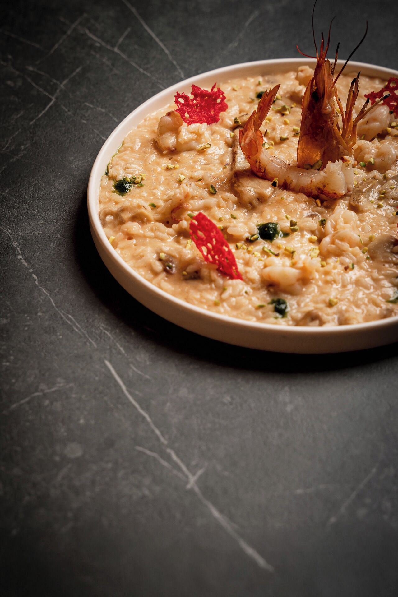 A plate of seafood risotto garnished with shrimp and red chili, served on a dark surface.