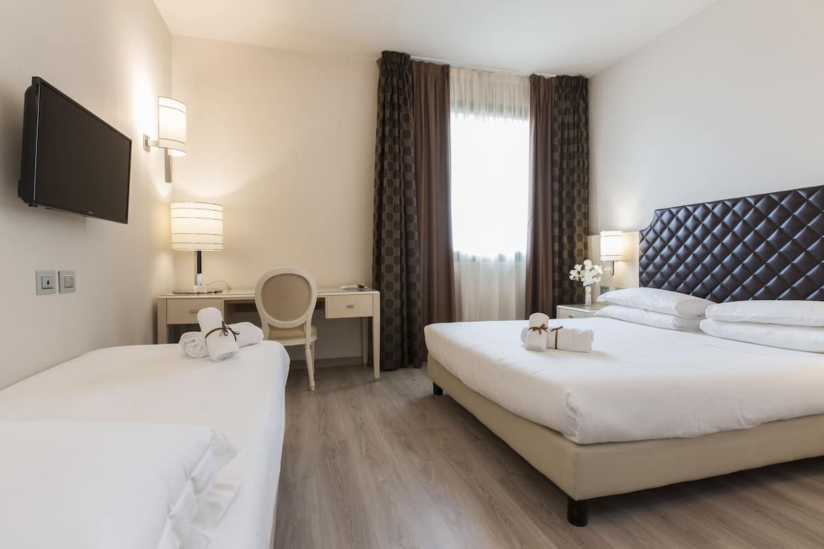 A hotel room with two beds, a desk, a chair, a TV, and a window with curtains.