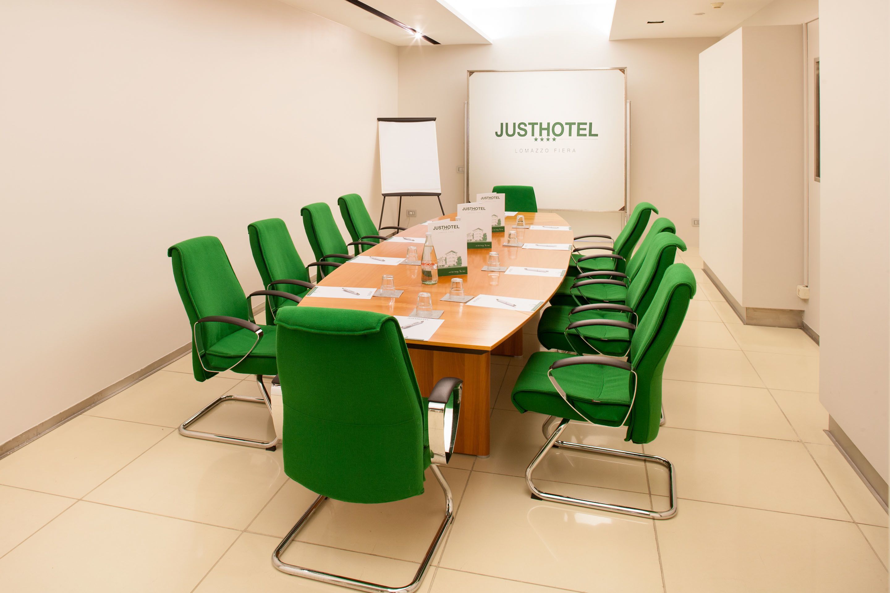 A conference room with a long table, green chairs, and a whiteboard with "JUSTHOTEL" branding.