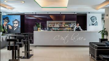 Un área de bar moderna con una barra que muestra 'C'est la vie' y un bartender. Hay taburetes de bar y un cuadro grande en la pared.