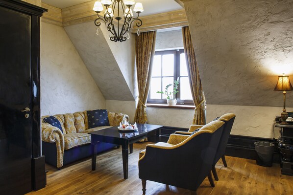 A room with a dark wooden floor, a blue sofa with patterned cushions, a black table with a white plate, and a chandelier.