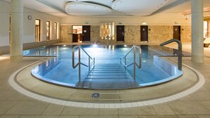 A large indoor swimming pool with a central staircase, stone walls, and a modern ceiling design.