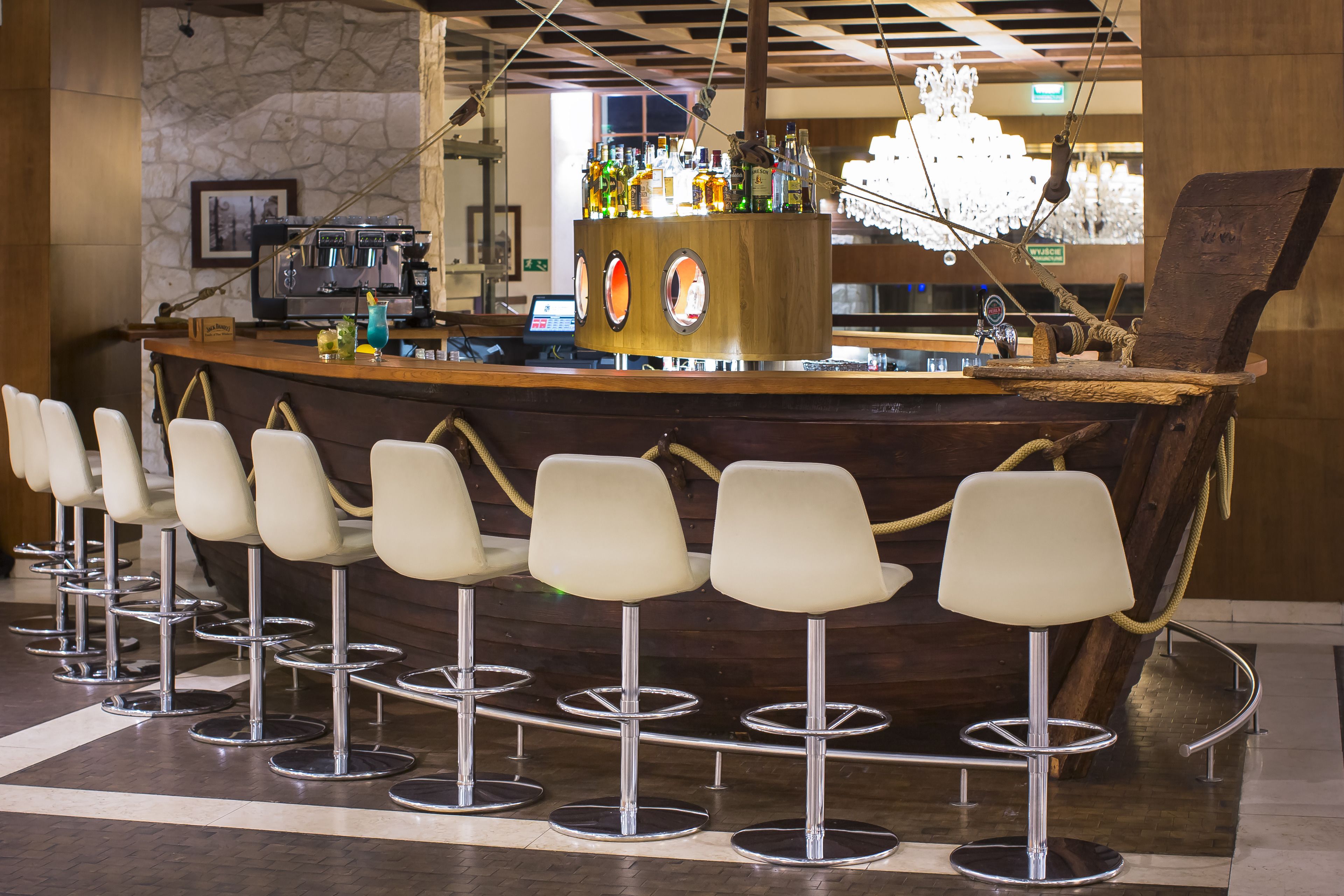 Una zona de bar con mostrador de madera, varios taburetes y una amplia variedad de botellas y vasos.