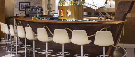 Una zona de bar con mostrador de madera, varios taburetes y una amplia variedad de botellas y vasos.