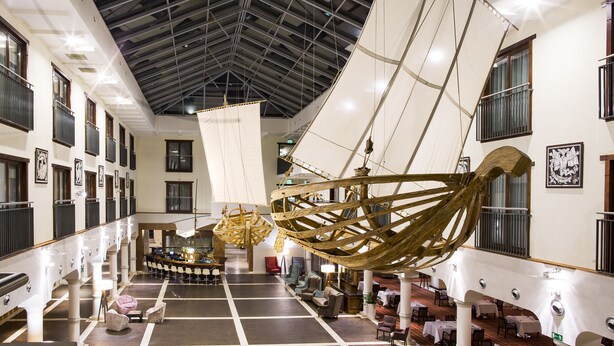 A spacious hotel lobby with a high ceiling, large windows, and a central seating area.