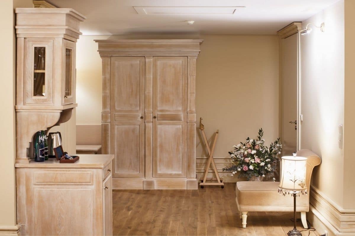 Ein Zimmer mit einem Holzkasten, einem großen Kleiderschrank, einer kleinen Bank und einer Lampe.