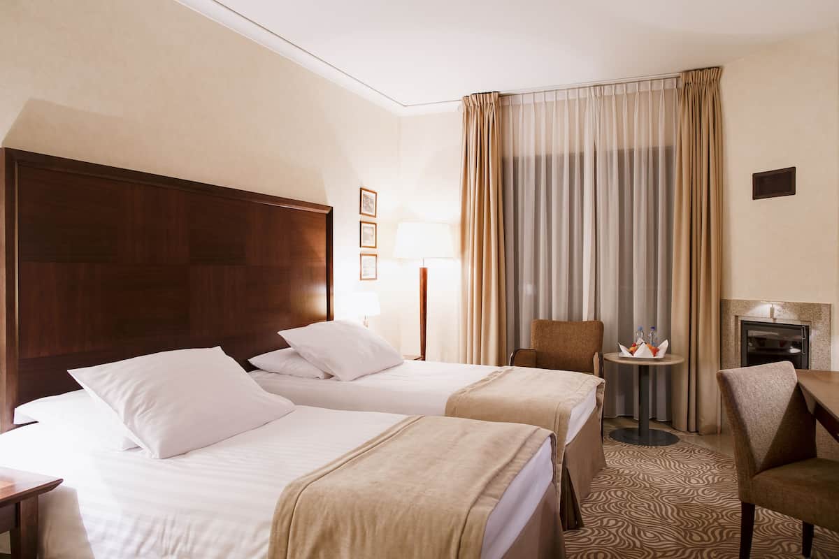 Ein Hotelzimmer mit zwei Betten, einem Schreibtisch, einem Stuhl, einer Lampe und einem kleinen Tisch mit Flaschen.