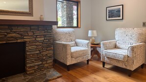 A cozy living room with a stone fireplace, two patterned armchairs, a small side table with a lamp, and a framed picture on the wall. - Wanaka Springs Lodge (Wanaka)