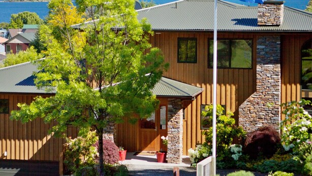 A wooden house with a stone facade, a flagpole with a flag, and a view of snow-capped mountains. - Wanaka Springs Lodge (Wanaka)