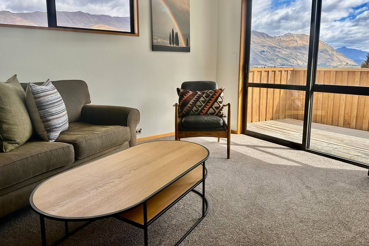 A living room with a sofa, a chair, a coffee table, and a large window with a view of mountains.