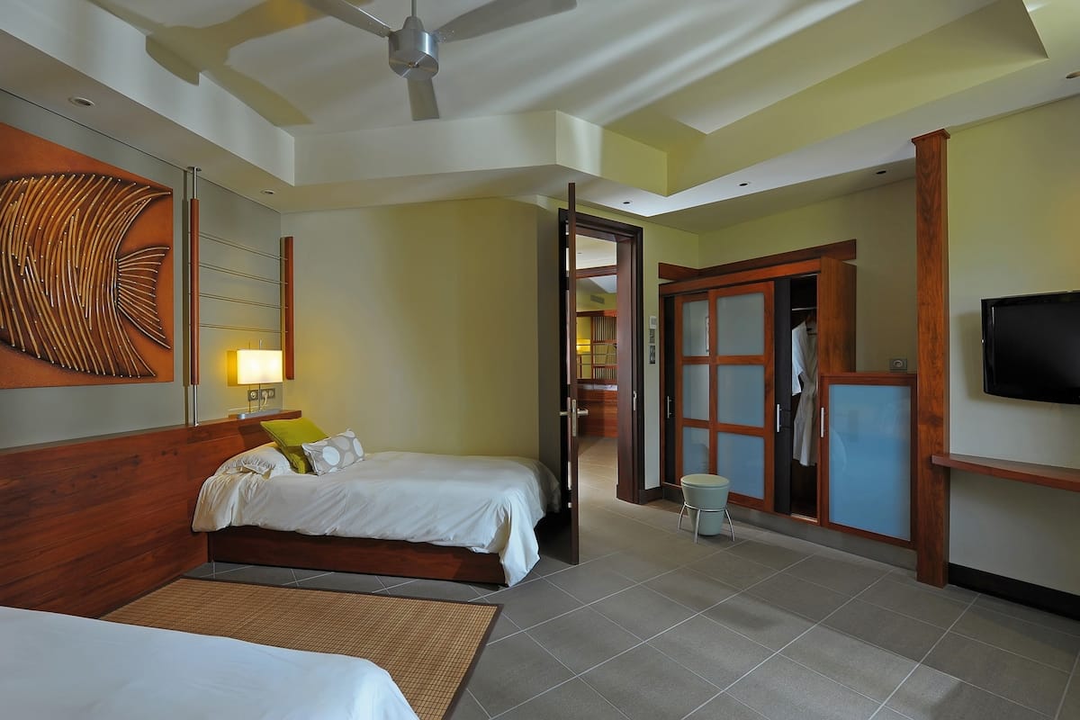 A hotel room with a bed, a television, a ceiling fan, and a wooden headboard.
