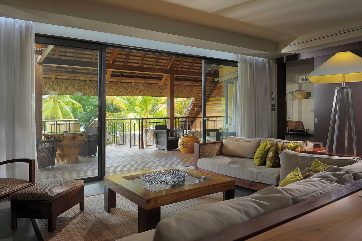 A spacious living area with a large sliding glass door leading to a balcony with a thatched roof and outdoor furniture.