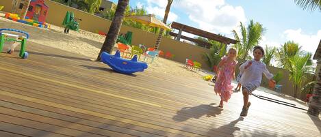 Una terraza de madera con estructuras de juego y palmeras.