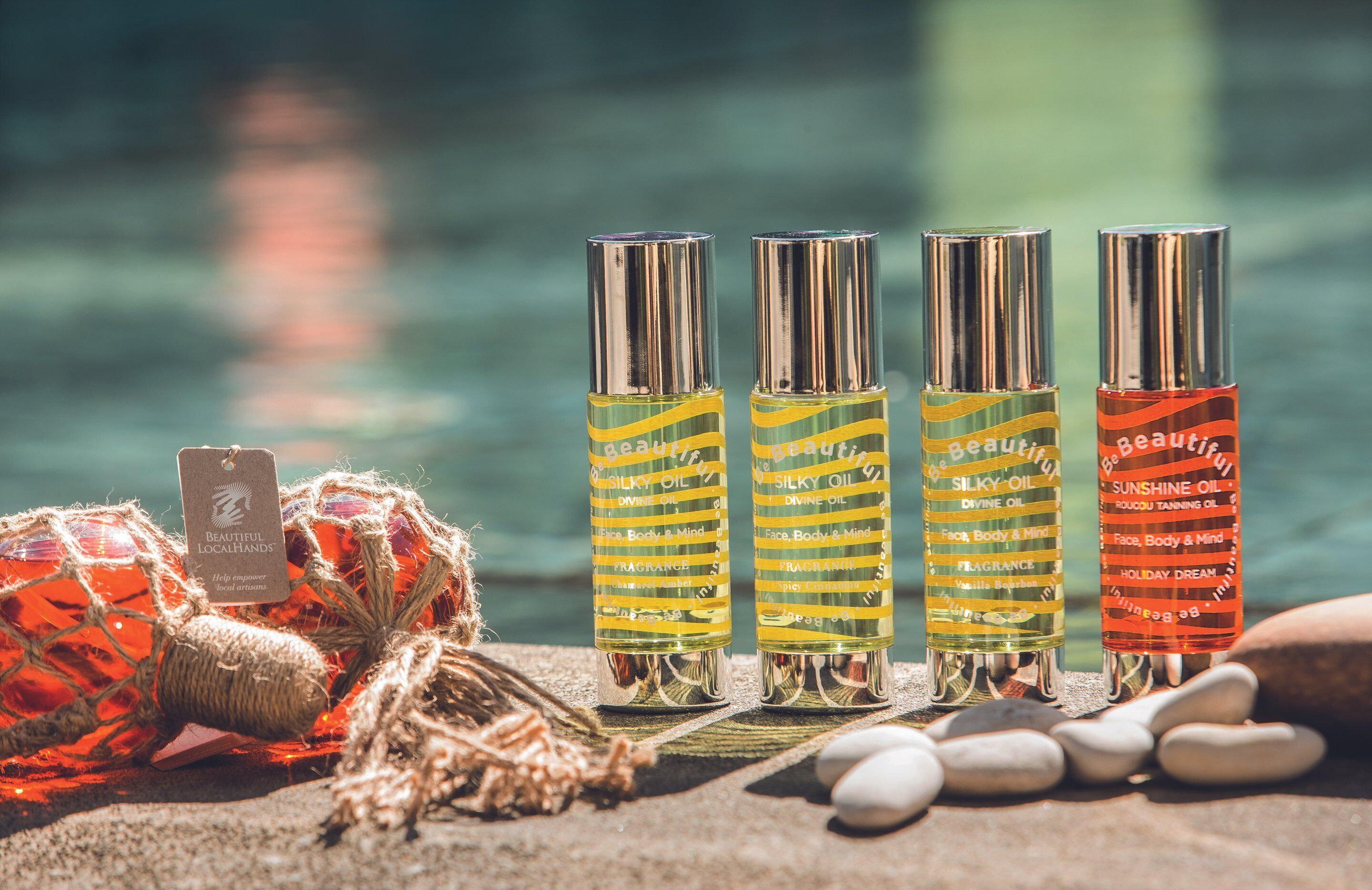 Four bottles of Silky Oil Divine Oil arranged on a stone surface with a blurred water background.