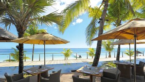An outdoor dining area with tables and chairs, umbrellas, and a view of the ocean. - Trou aux Biches Beachcomber Golf Resort & Spa (Trou aux Biches)
