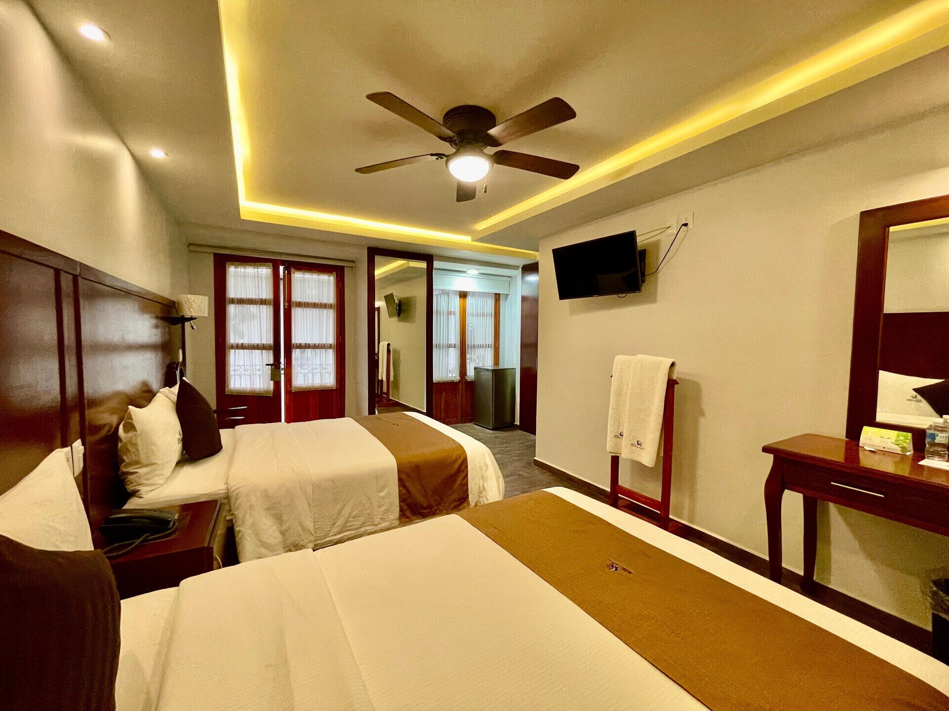 A hotel room with two beds, a ceiling fan, a TV, and a bathroom visible through an open door.
