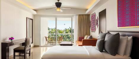 Habitación de hotel con cama, escritorio, sillón, sofá y balcón con vista a palmeras.