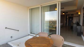 A balcony with a glass door, a wooden table, two wicker chairs, and a view of a cityscape.