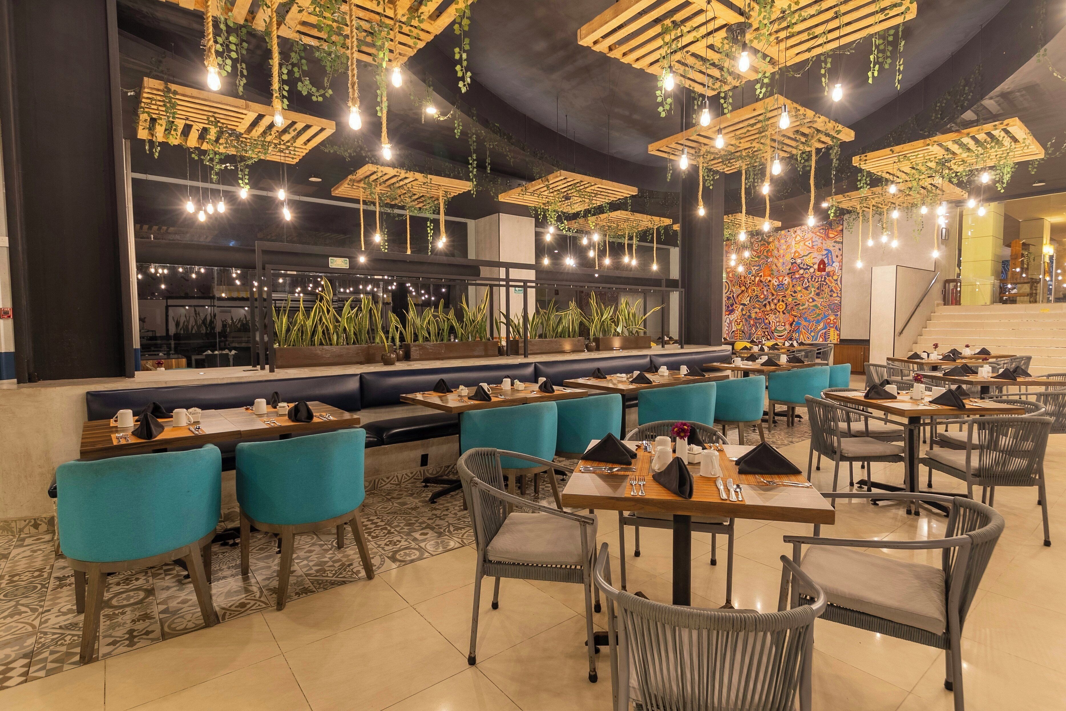 A restaurant with multiple seating areas, including booths and tables, with hanging light fixtures and plants.